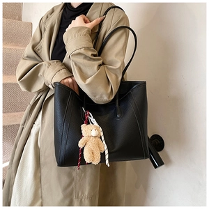Close-up of a black lychee texture leather tote bag with a cute bear charm and striped ribbon