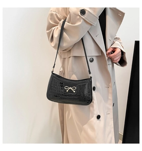 Détail du sac baguette noir texture croco avec boucle nœud doré porté par mannequin