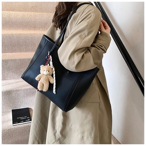 Litchi texture black tote bag with plush bear charm and ribbon on model's shoulder