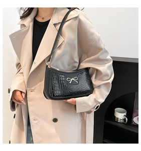 Détail du sac à bandoulière noir motif crocodile avec un nœud doré métallique