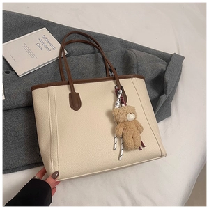 Detail of cream pebbled leather tote bag with brown handles and plush bear charm