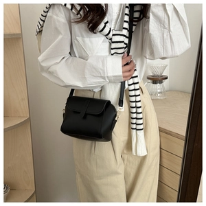Detail view of a black matte leather crossbody bag with flap and gold metal hardware