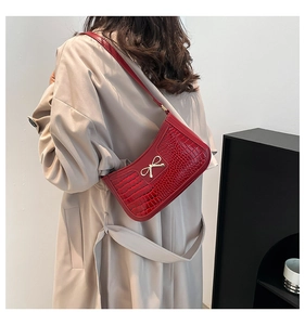 Détail d'un sac à bandoulière rouge motif crocodile avec un nœud doré en métal