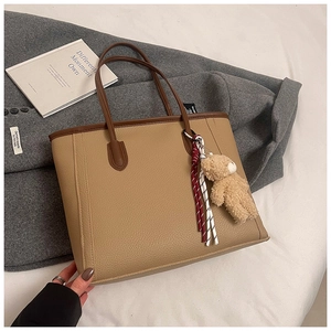 Detail of khaki pebbled leather tote bag with brown handles and plush bear charm