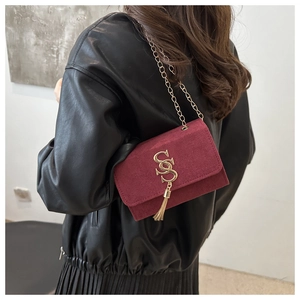 Detail of burgundy suede chain bag with golden tassel and S-shaped buckle on model
