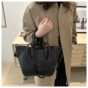 Detail of black pebbled leather tote bag with contrast stitching and long handles