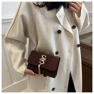 Detailed view of coffee brown suede mini crossbody bag with gold chain and tassel on model