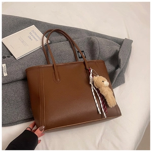 Detail of brown litchi pattern leather tote bag with a cute plush bear pendant on coat