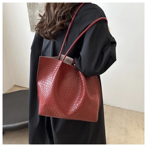 Detail view of burgundy woven tote bag with square textured leather and shoulder straps