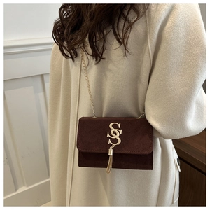 Detail of burgundy suede crossbody bag with gold chain and fringe on model coat