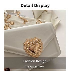 Détail d'un sac enveloppe en cuir crème avec boucle cœur dorée et ornements de perles