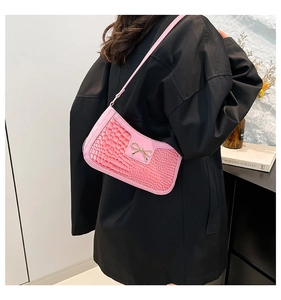 Détail du sac baguette rose à motif crocodile avec nœud doré porté sur un manteau noir