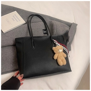 Detail of black lychee grain leather tote bag featuring a cute teddy bear charm