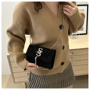 Fashionable black suede crossbody bag with gold chain strap worn by a model in soft lighting