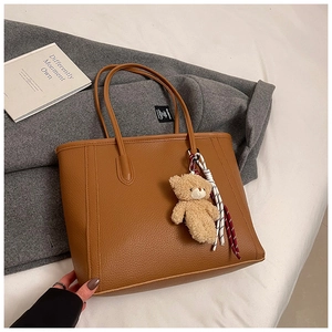 Detail of brown lychee texture leather tote bag with a cute plush bear charm accessory