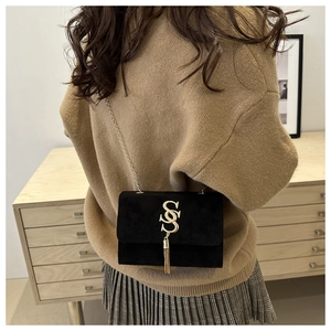 Detail of black suede shoulder bag featuring a gold S-logo with decorative metal tassels