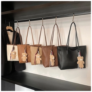 Multiple textured tote bags with bear charms and striped ribbons hanging in a closet