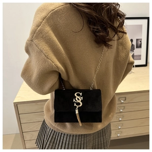 Close-up of black suede crossbody bag with gold S-logo and chain strap on a model