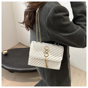 Detail of white quilted leather bag with gold S-logo and fringe tassel on corduroy coat