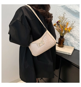 Détail du sac beige en cuir gaufré crocodile avec nœud doré et forme de demi-lune