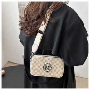 Detail of beige camera bag with M-pattern monogram and silver metal logo on a wide strap