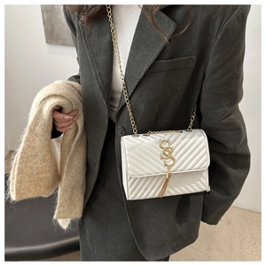 Detail of cream quilted crossbody bag with golden logo and tassel chain strap