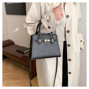 Detail of black trapezoid handbag with gold rotating lock and crossbody strap shown on model