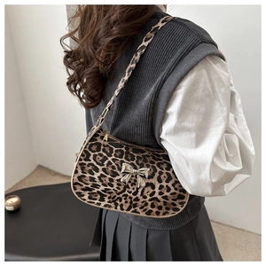 Detail of leopard print baguette bag with metallic bow charm worn on the shoulder