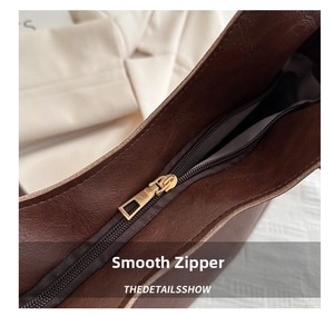 Detail of smooth gold zipper and brown leather texture on a stylish tote bag