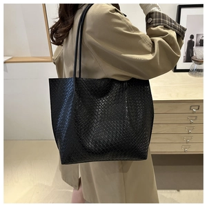 Close-up of black woven texture tote bag with long shoulder strap in a modern home setting