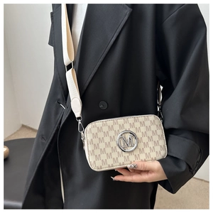 Close-up of cream monogram camera bag with M-logo and wide webbing strap on black blazer