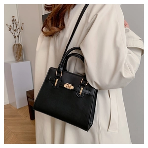 Detail of black structured kelly bag with golden twist lock and adjustable shoulder strap