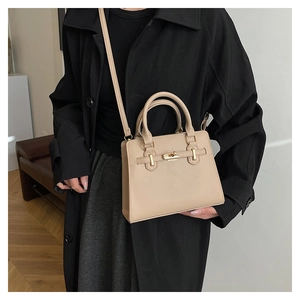Close-up of stylish beige trapezoid tote bag with gold buckle hardware on dark coat