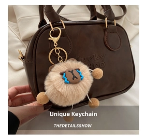 Close-up of a brown fuzzy plush charm with cartoon face on a dark leather bag