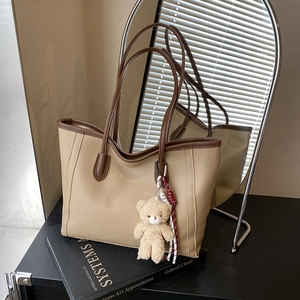 Chic beige textured tote bag with brown straps and plush bear charm on art books