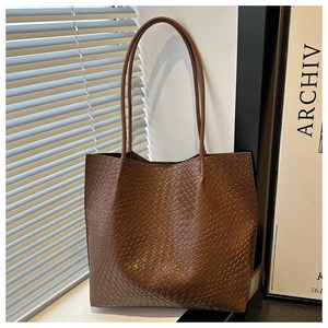 Detail of a brown tote bag with woven texture and long shoulder straps for daily use