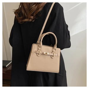 Fashionable beige tote bag with gold hardware worn as a crossbody bag over a black coat
