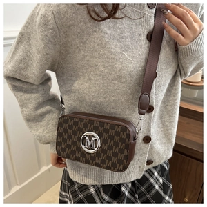Detail of a brown camera bag featuring an M monogram print and a round metallic logo