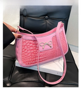 Détail de la texture en cuir rose gaufré crocodile avec un nœud doré sur le sac baguette