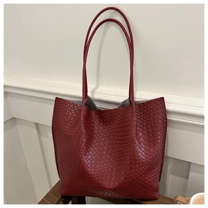 Detail of burgundy woven tote bag with long straps on dark wood surface in room setting