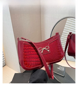 Détail d'un sac à main rouge à texture crocodile avec boucle decorative en nœud doré