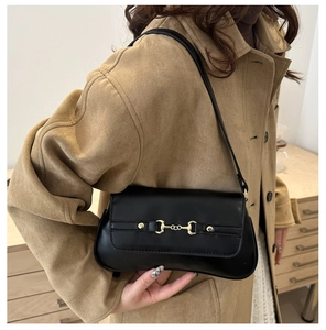 Détail du sac à bandoulière en cuir noir avec boucle mors dorée sur manteau beige