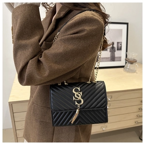 Close-up of black V-quilted leather handbag with gold metal logo and tassel detail