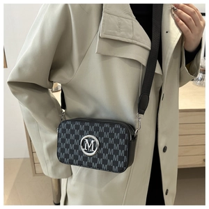 Detail of trendy black crossbody camera bag with grey M pattern and silver logo on a model
