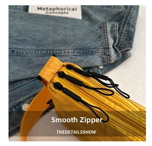 Detail view of smooth zippers and three storage compartments on a yellow crossbody bag