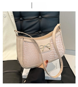 Gros plan du sac baguette kaki avec texture crocodile et nœud doré sur chaise en cuir