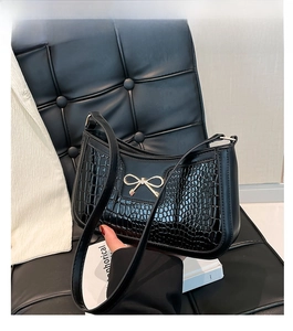 Détail du sac bandoulière noir motif crocodile avec nœud doré sur surface texturée
