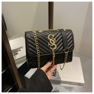 Detail of black V-quilted shoulder bag with gold monogram logo and metal tassel