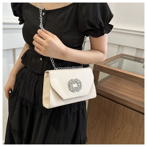 Close-up of white glossy crossbody bag featuring a crystal buckle and silver chain strap