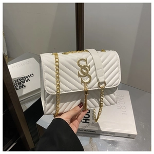 Close-up of a white quilted chain bag featuring a gold S-logo and fringe tassel detail